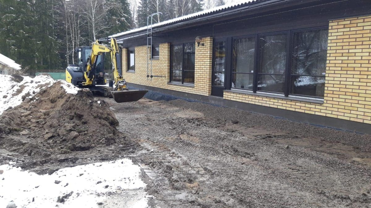 Pieni kaivuri keltaisen tillitalon vieressä